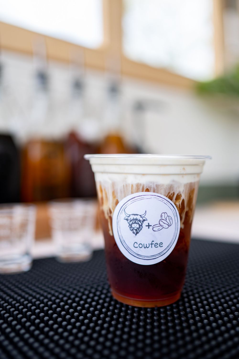 A cold brew coffee drink in a plastic cup with a unique bull and moon logo on a black mat.
