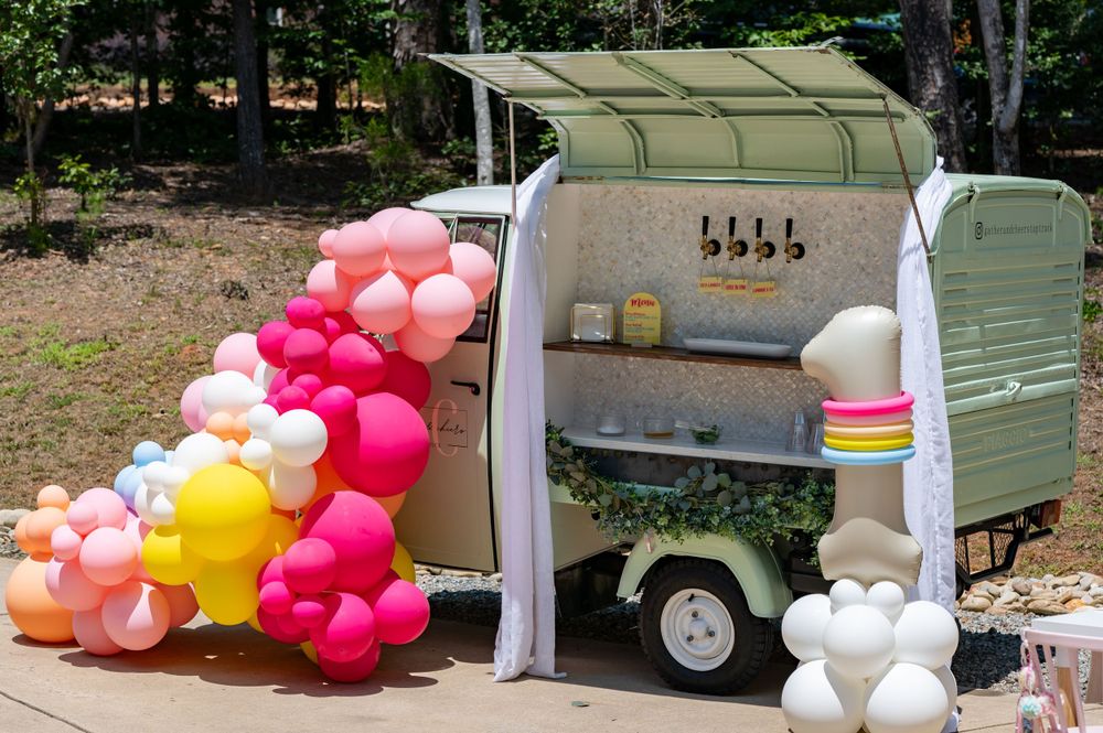 Mobile beverage cart decorated with colorful balloon arch and serving stations.