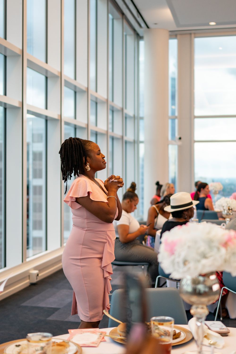 Woman in pink dress stands reflectively by floor-to-ceiling windows during an elegant event.