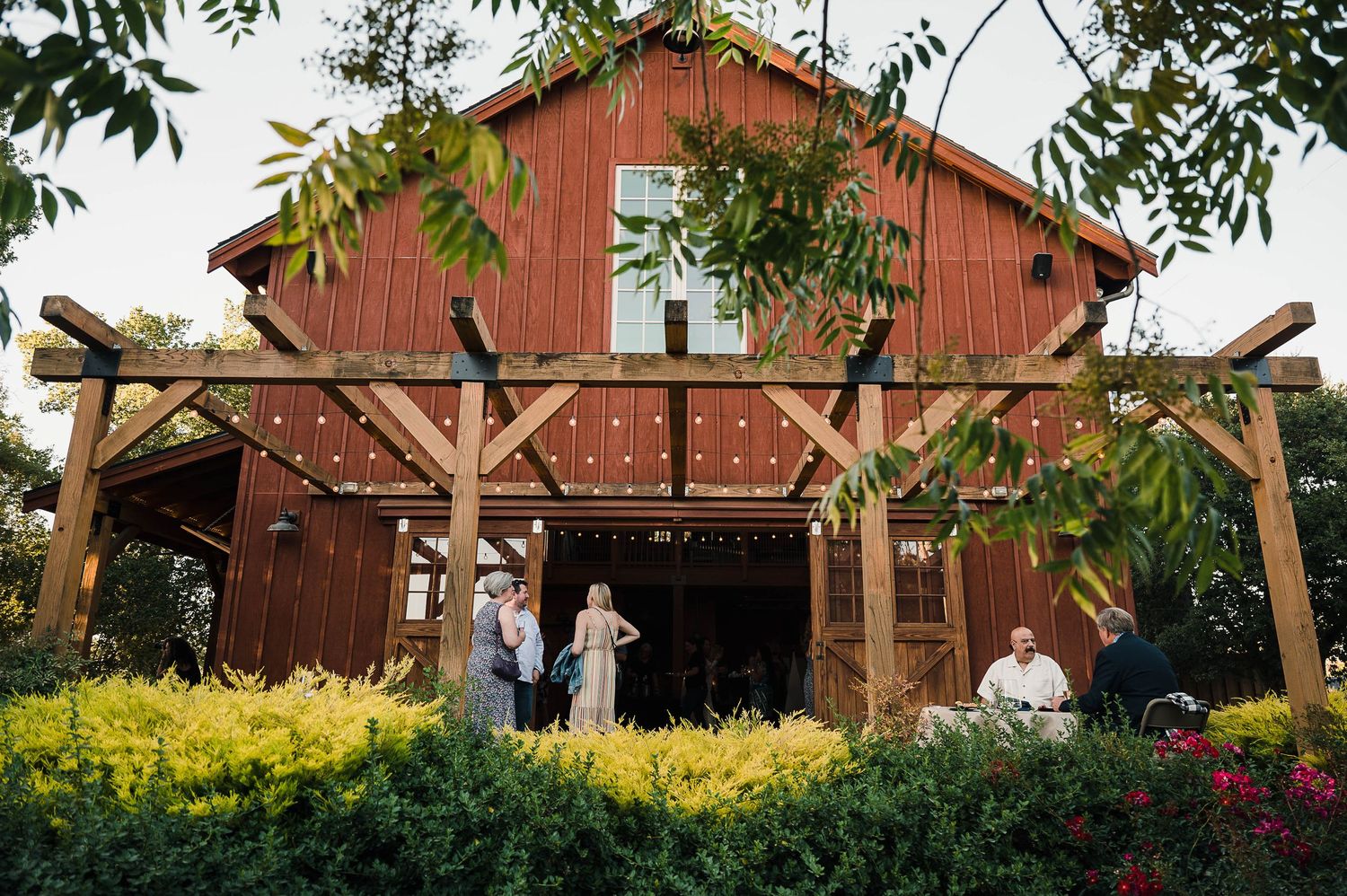 A rustic red barn wedding venue with wooden beams and colorful garden landscaping.