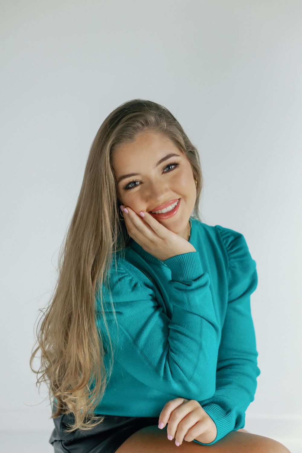 Playful portrait of someone in a teal sweater against a white background.