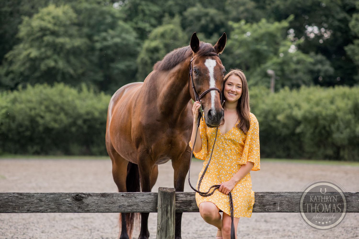 A brown horse and person in yellow dress pose together by a wooden fence during an outdoor photoshoot.