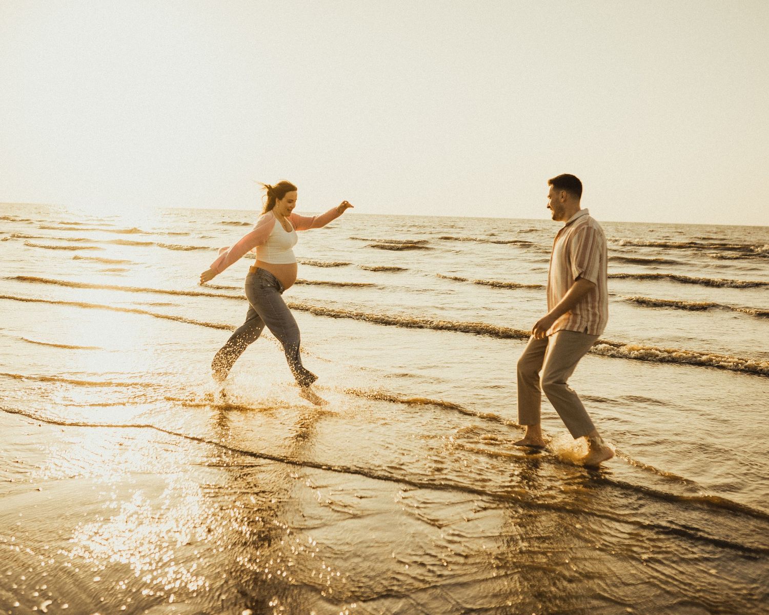 Couple splashing and playing in ocean waves during golden hour sunset.