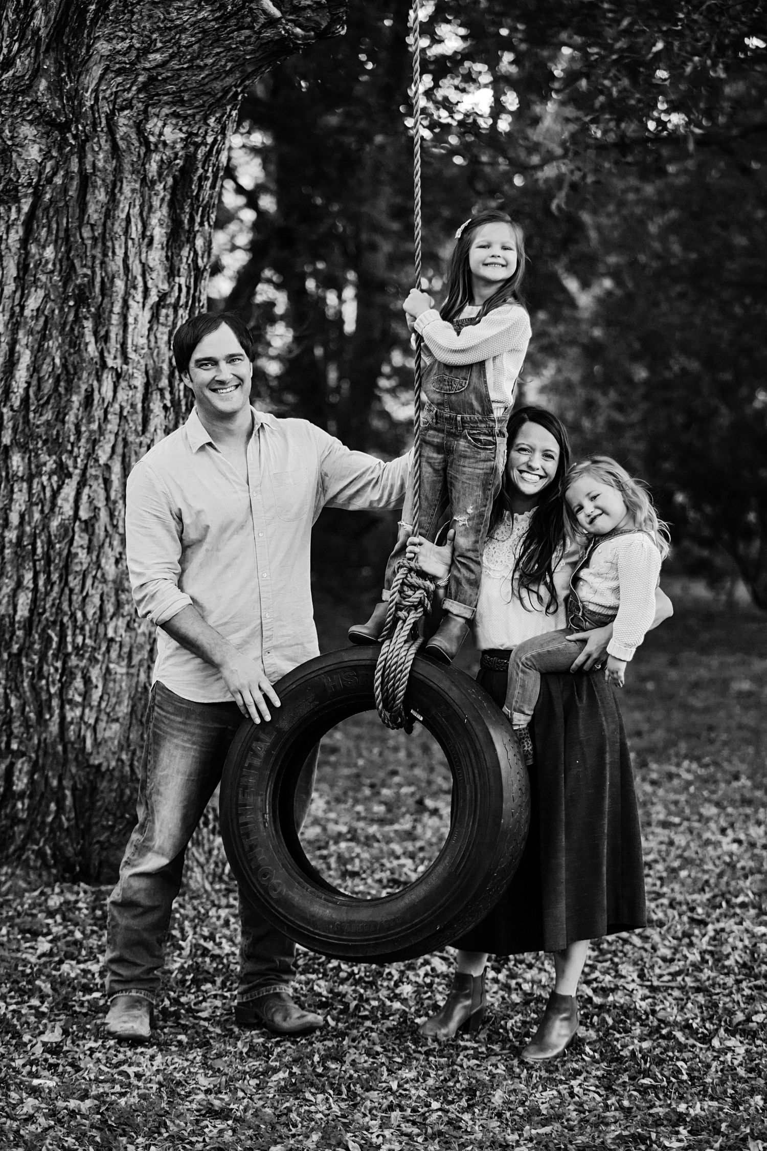 A family poses playfully around a tire swing hanging from a large tree.