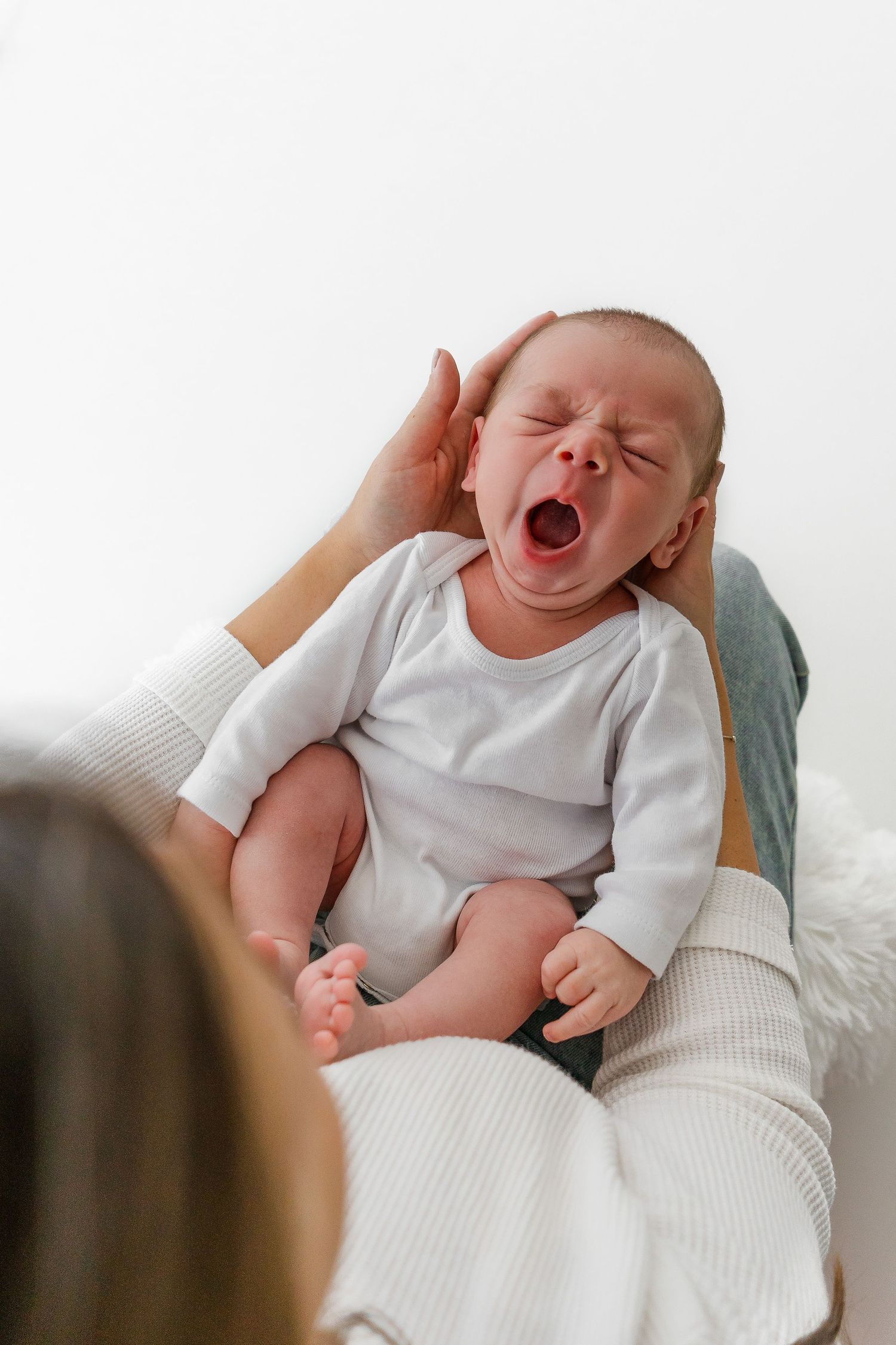 Baby yawning while lying on soft fabric against white background.
