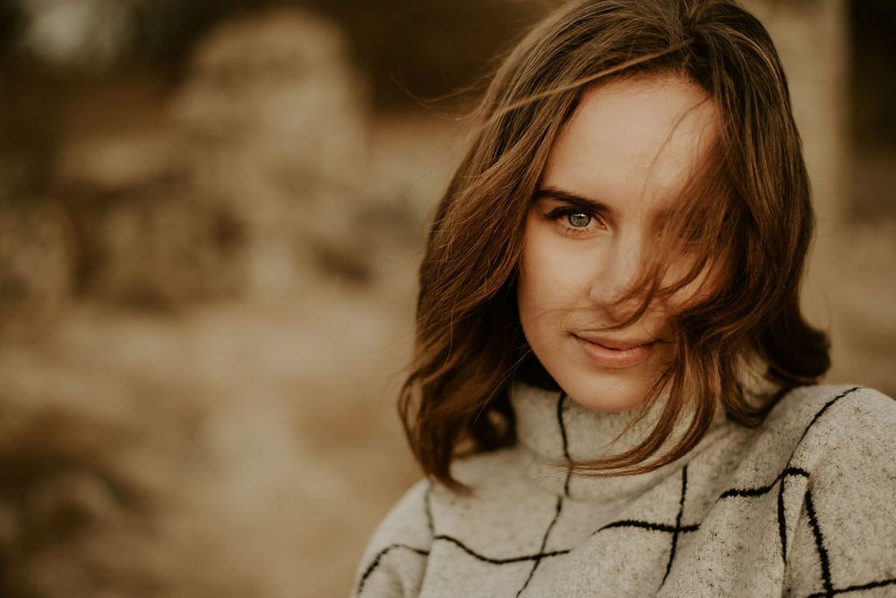 A candid portrait shot in sepia tones featuring windswept hair and a cozy sweater.