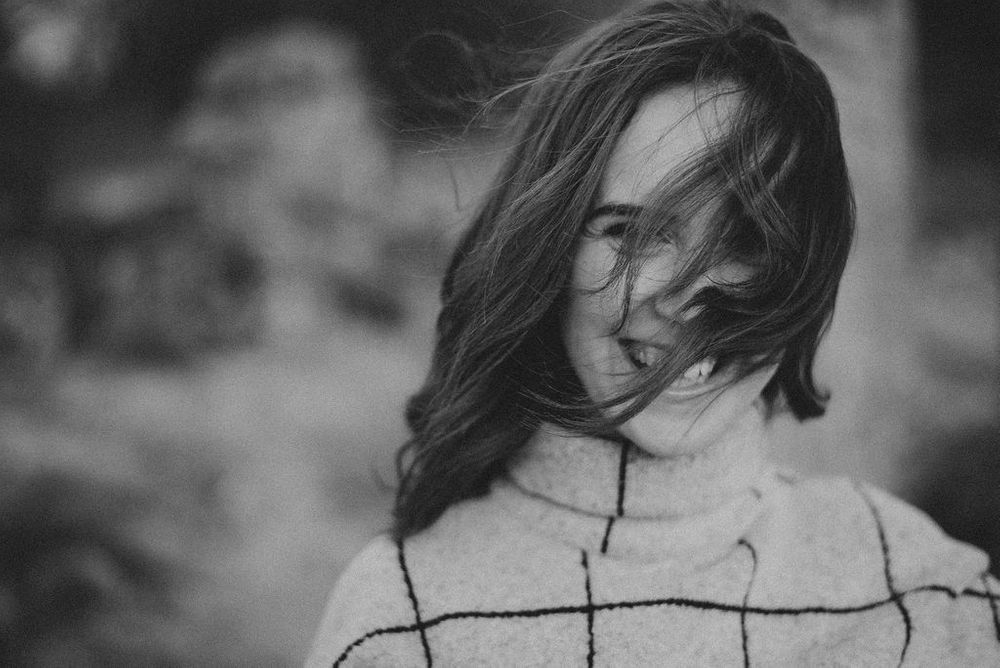 Close-up portrait with natural lighting showing a gentle smile and textured knit sweater.