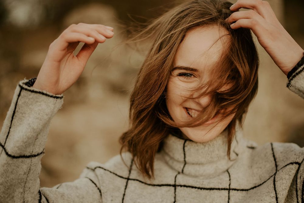 Playful outdoor portrait with wind-tousled hair and geometric patterned sweater.
