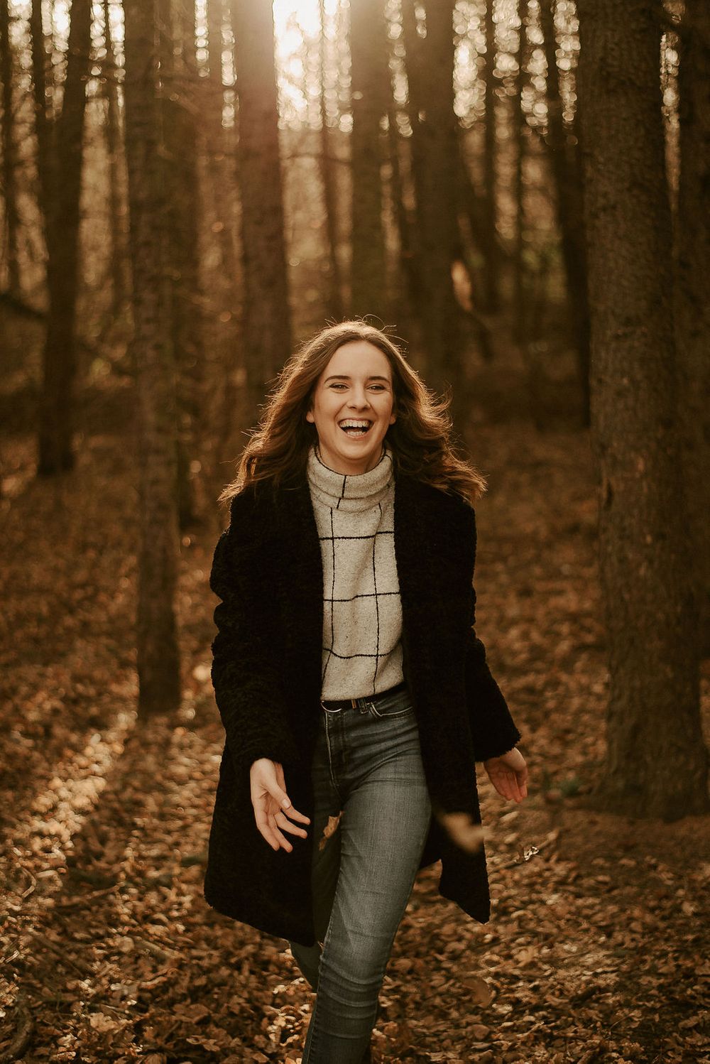 Joyful movement captured in autumn forest wearing black coat and plaid sweater.