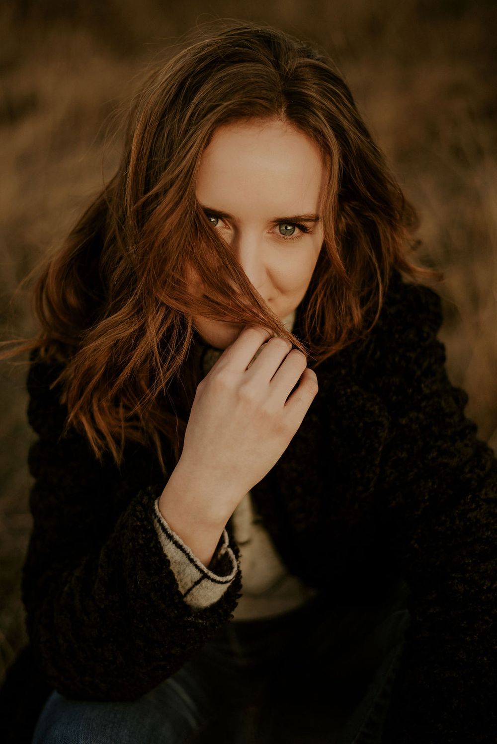 A moody portrait in warm tones featuring someone in a black sweater with flowing brown hair.