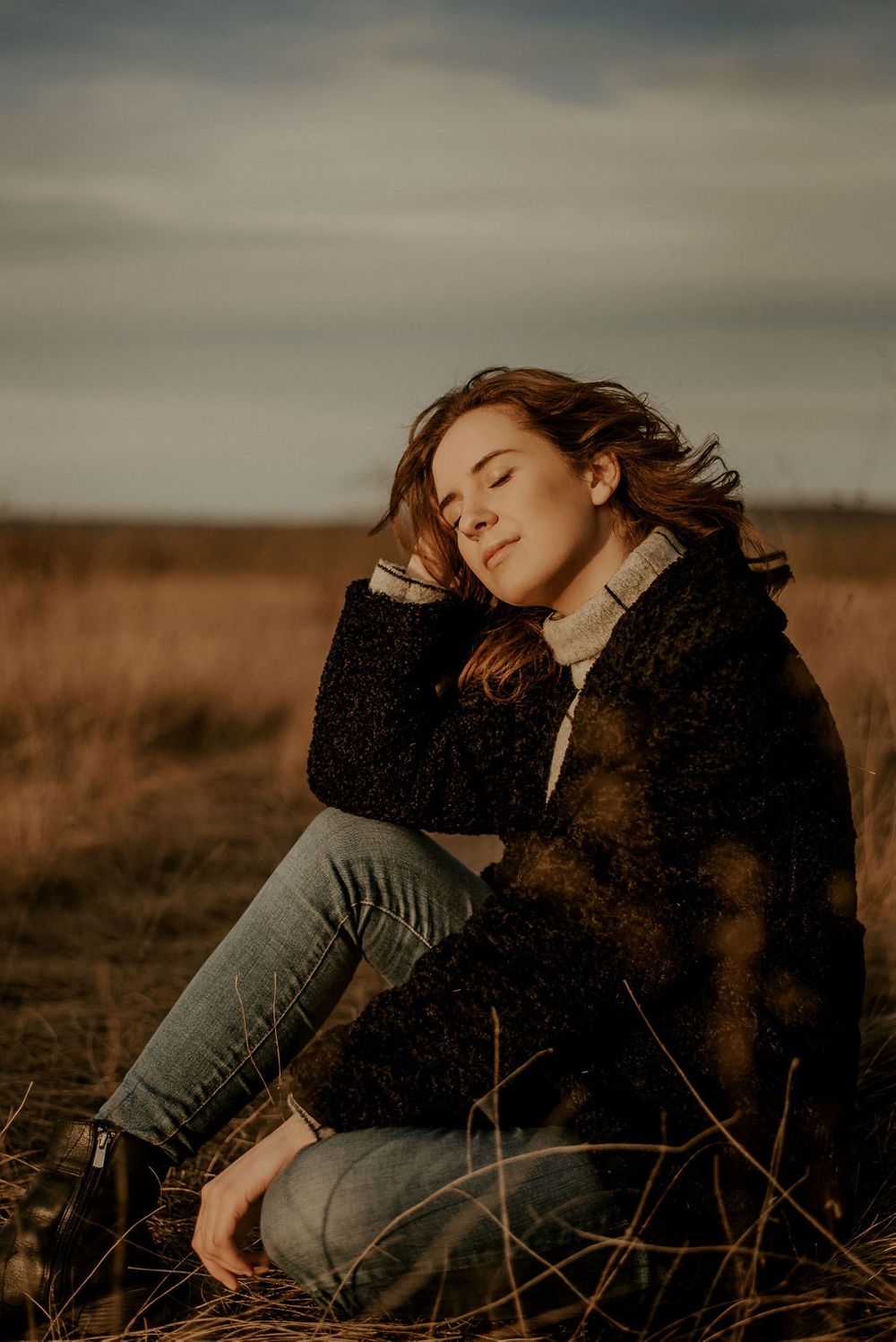 Person in black sweater lying peacefully in autumn field during golden hour.