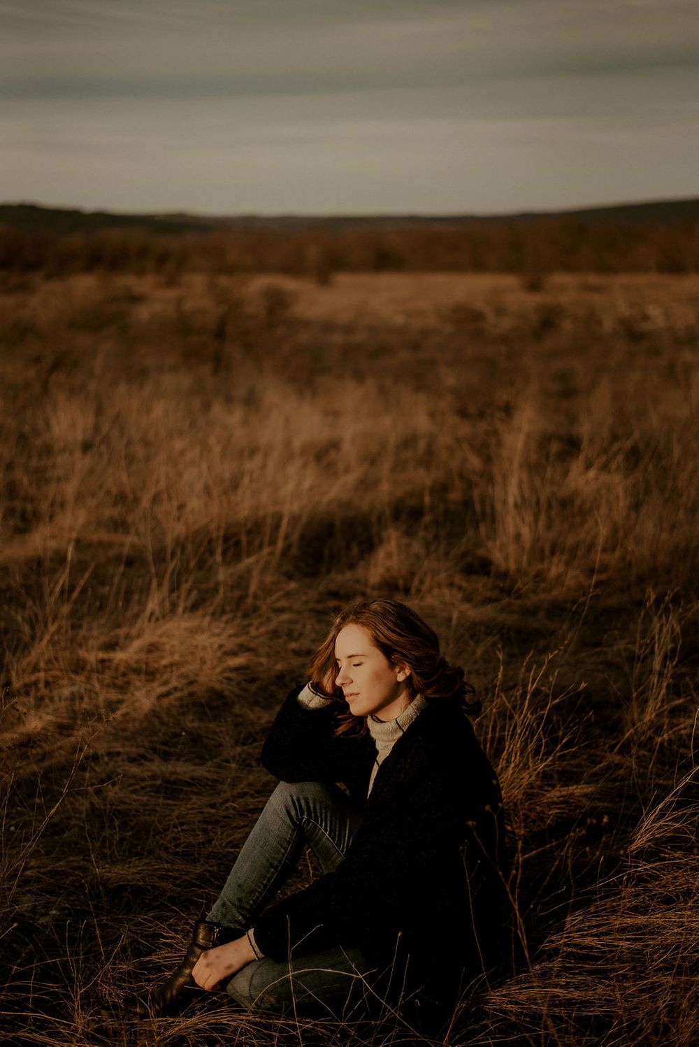 A contemplative portrait of someone sitting in dry grass during golden hour.