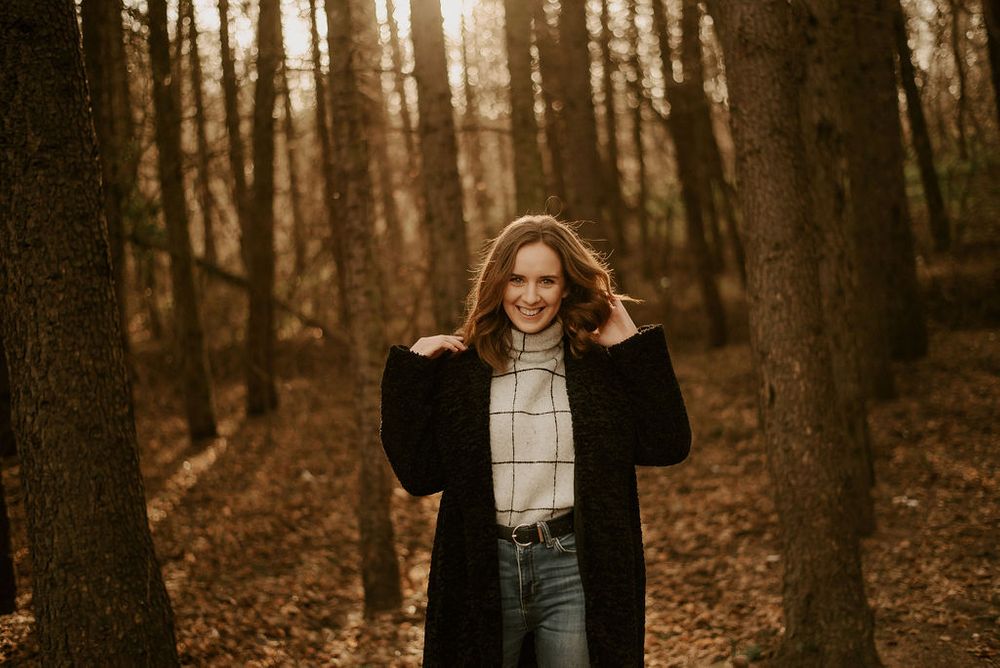 Autumn forest photoshoot featuring casual outfit with black coat and white top.