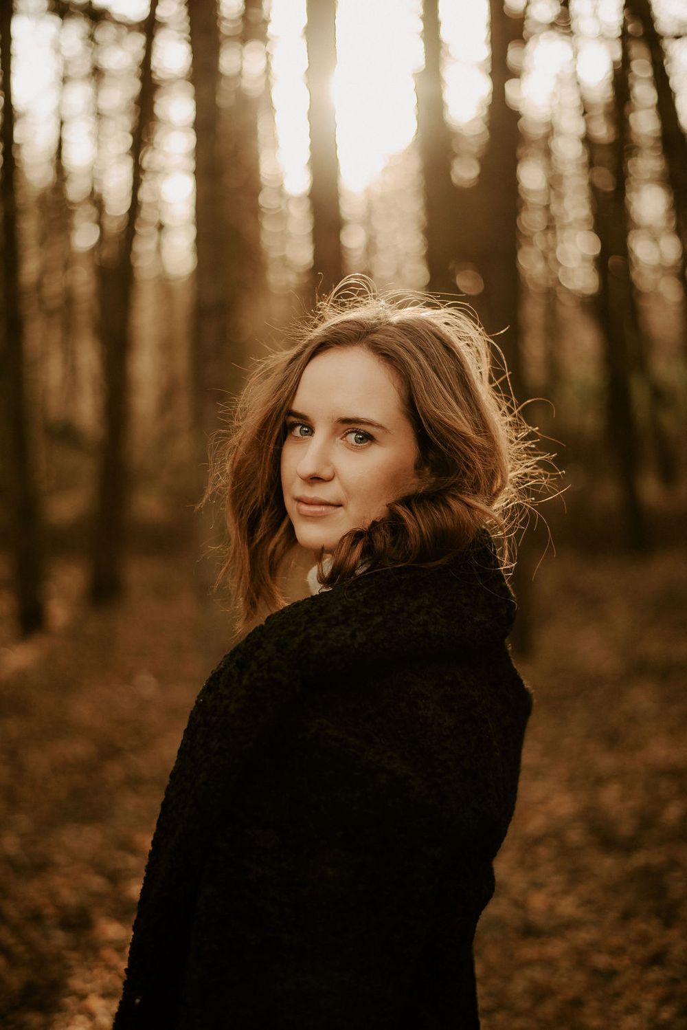 Moody forest photoshoot featuring black winter coat and natural lighting through trees.