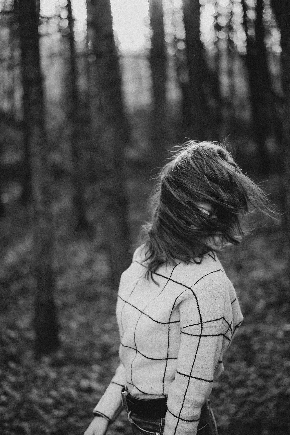 Dynamic black and white portrait with motion-blurred hair in forest setting.