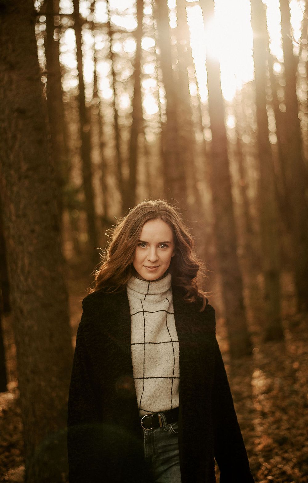 Moody forest portrait featuring black coat and plaid top during golden hour.
