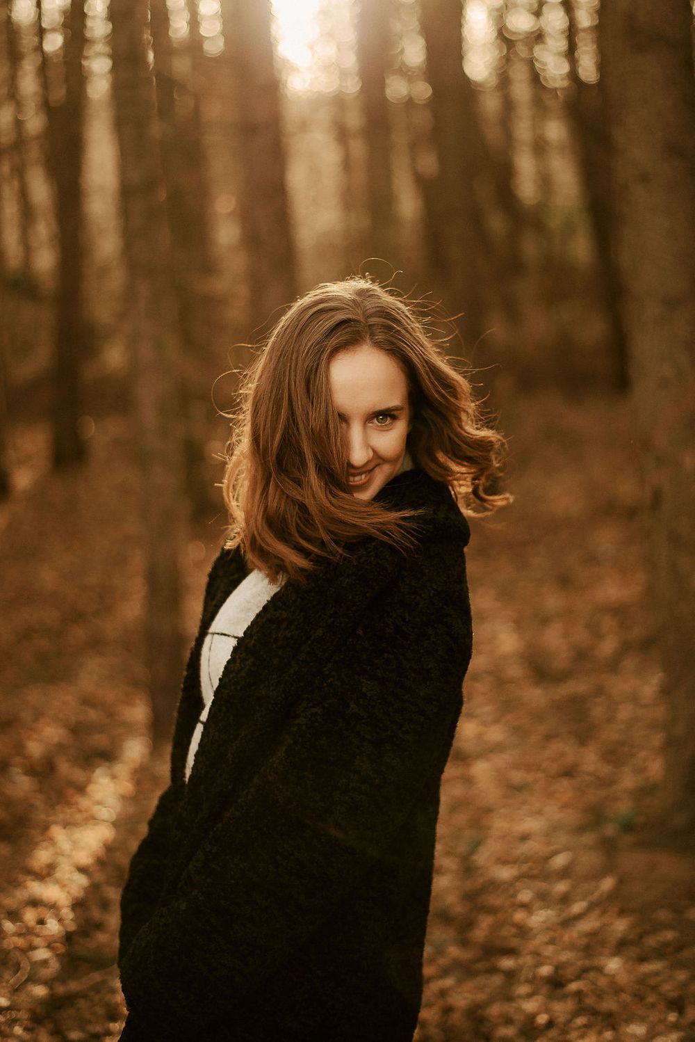 Dramatic autumn portrait with wind-swept hair in wooded setting.