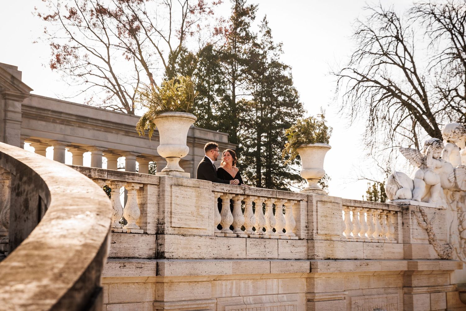 Romantic couple leaning together on an ornate stone balustrade at a historic estate.