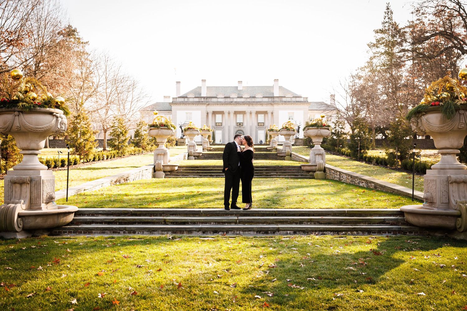Couple embracing on garden steps with a grand historic mansion in the background.