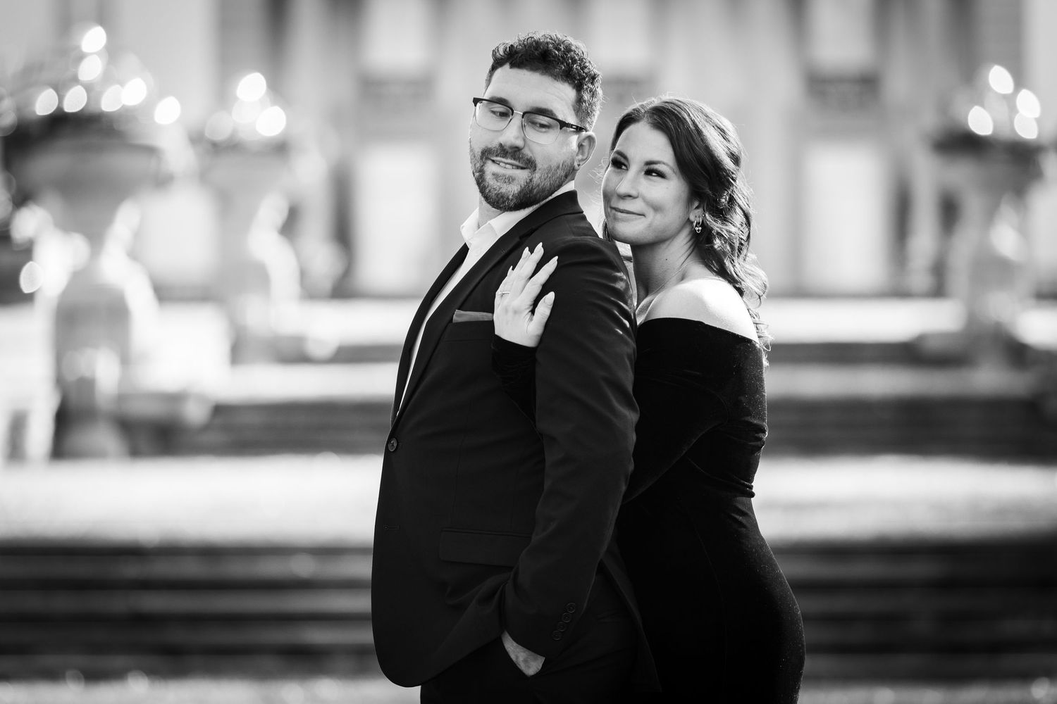 Black and white portrait of a couple posing back to back in elegant formal wear.