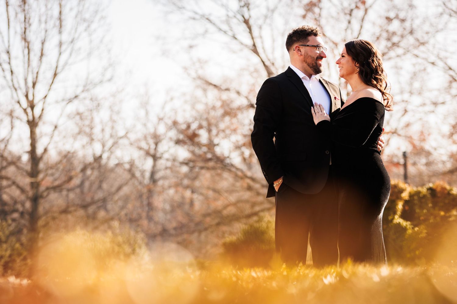 Couple in formal attire sharing a tender moment surrounded by golden autumn foliage.