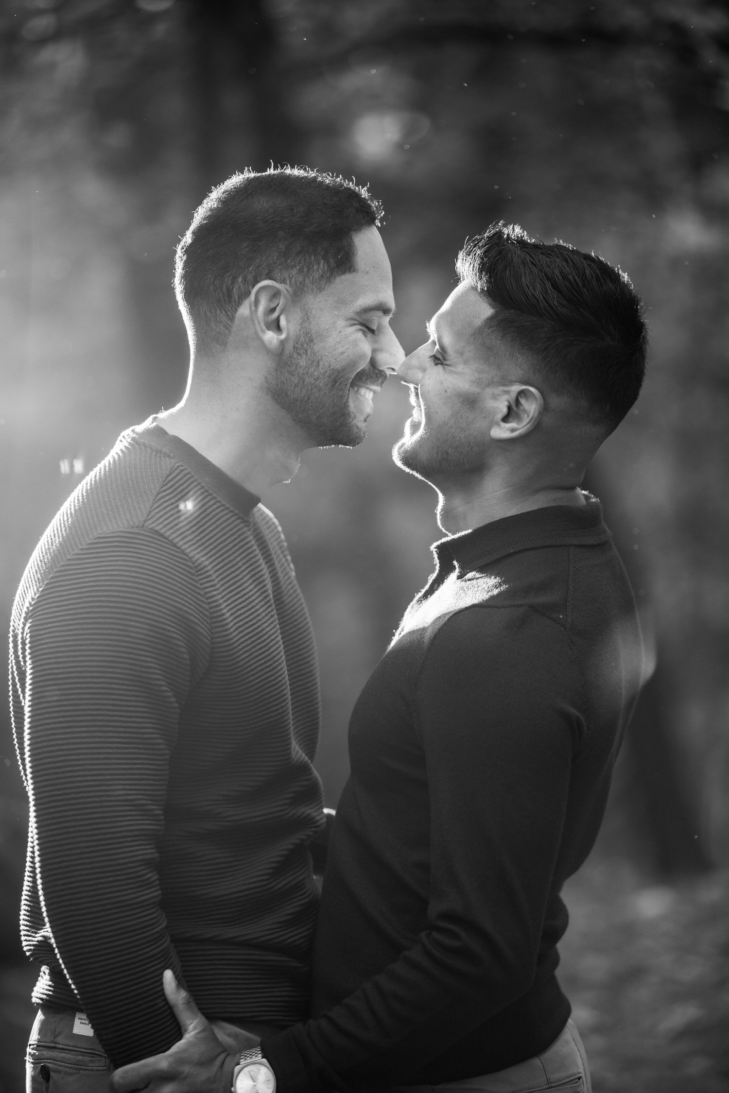 Two men smile and touch noses in a tender black and white romantic portrait outdoors.