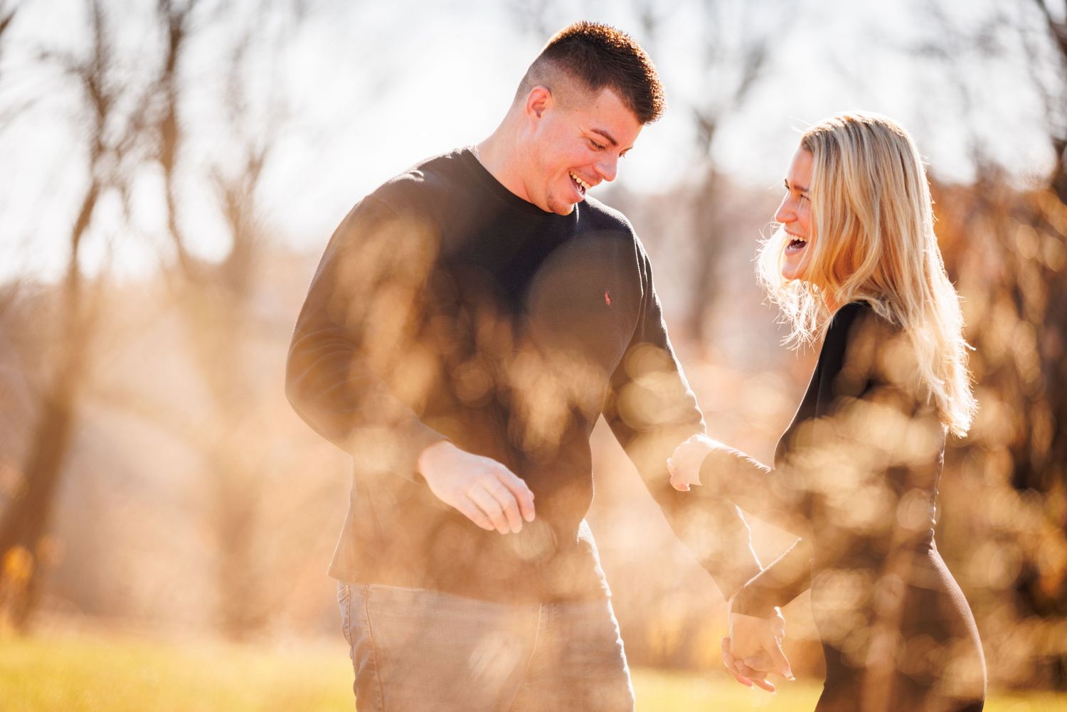 Laughing couple holding hands in sunlit autumn park with golden bokeh background.