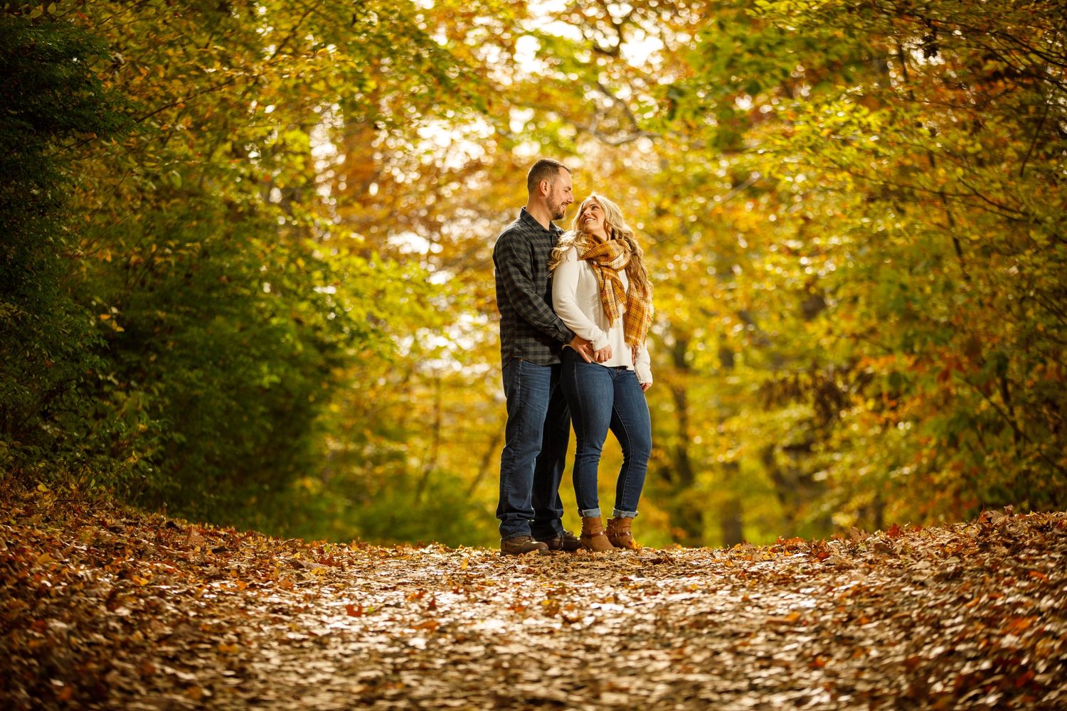 Romantic couple embracing on a scenic fall forest path covered in golden autumn leaves.