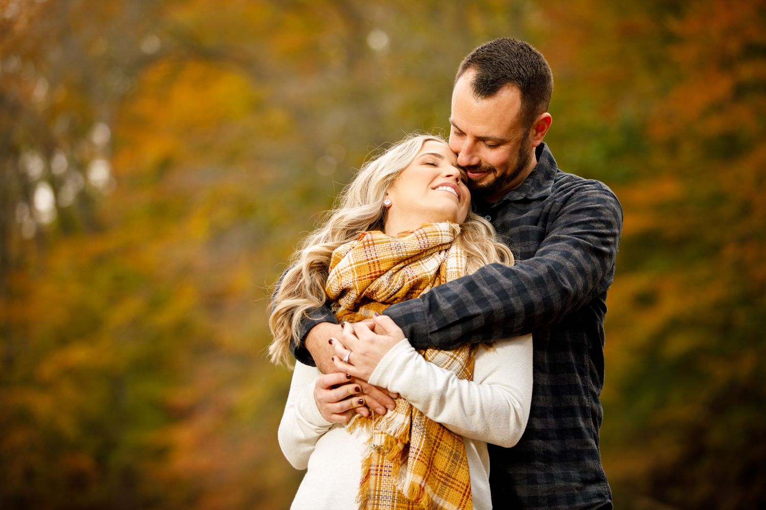 Man tenderly embracing woman from behind in a colorful autumn forest setting.