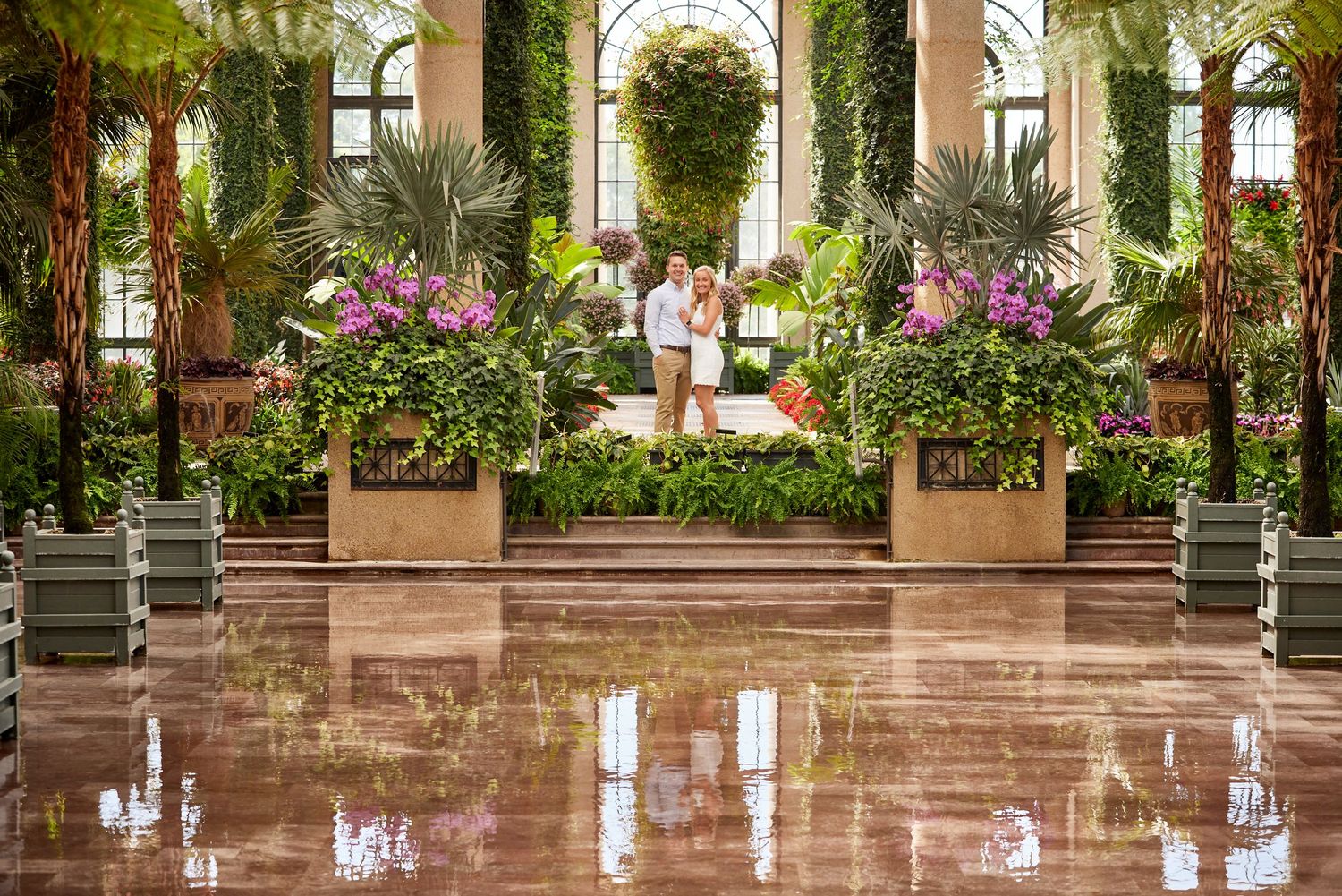 Couple standing together in stunning greenhouse conservatory surrounded by tropical flowers.