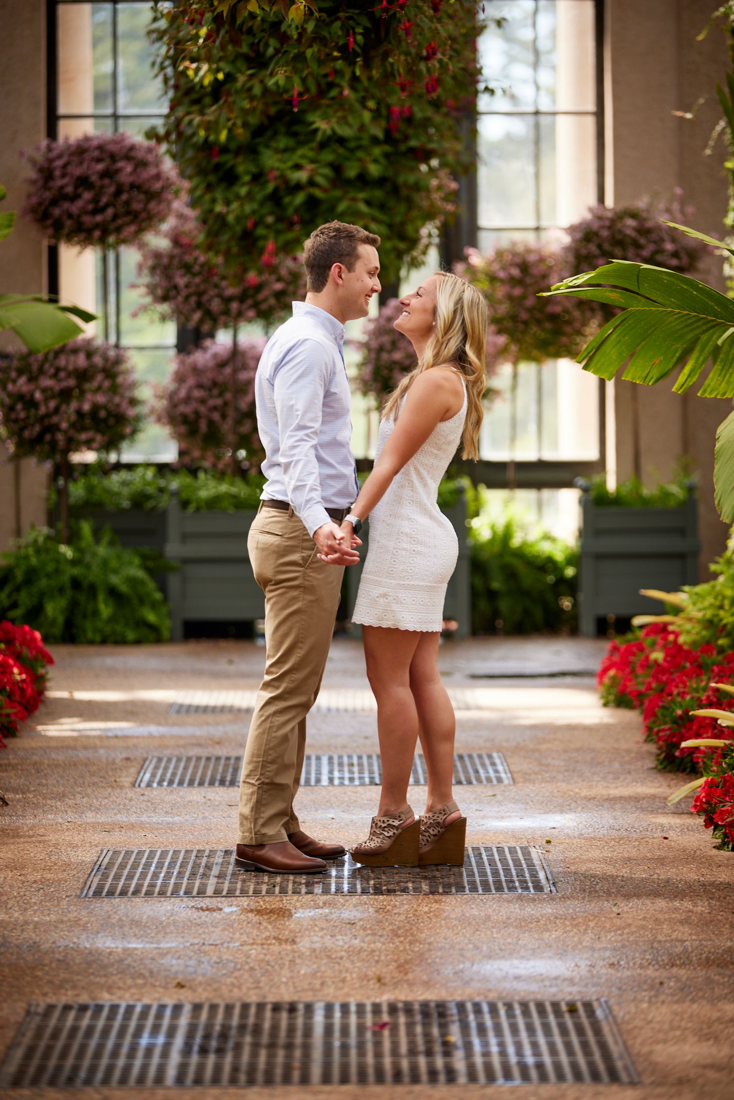Couple about to kiss while standing on garden path surrounded by colorful flowers.