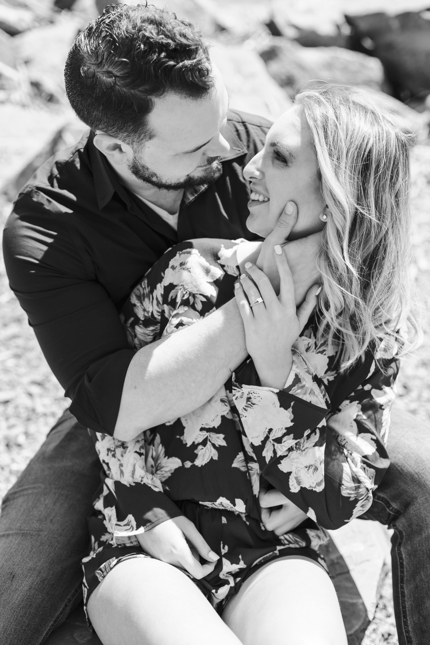 Black and white photo of couple sitting closely, gazing lovingly at each other outdoors.