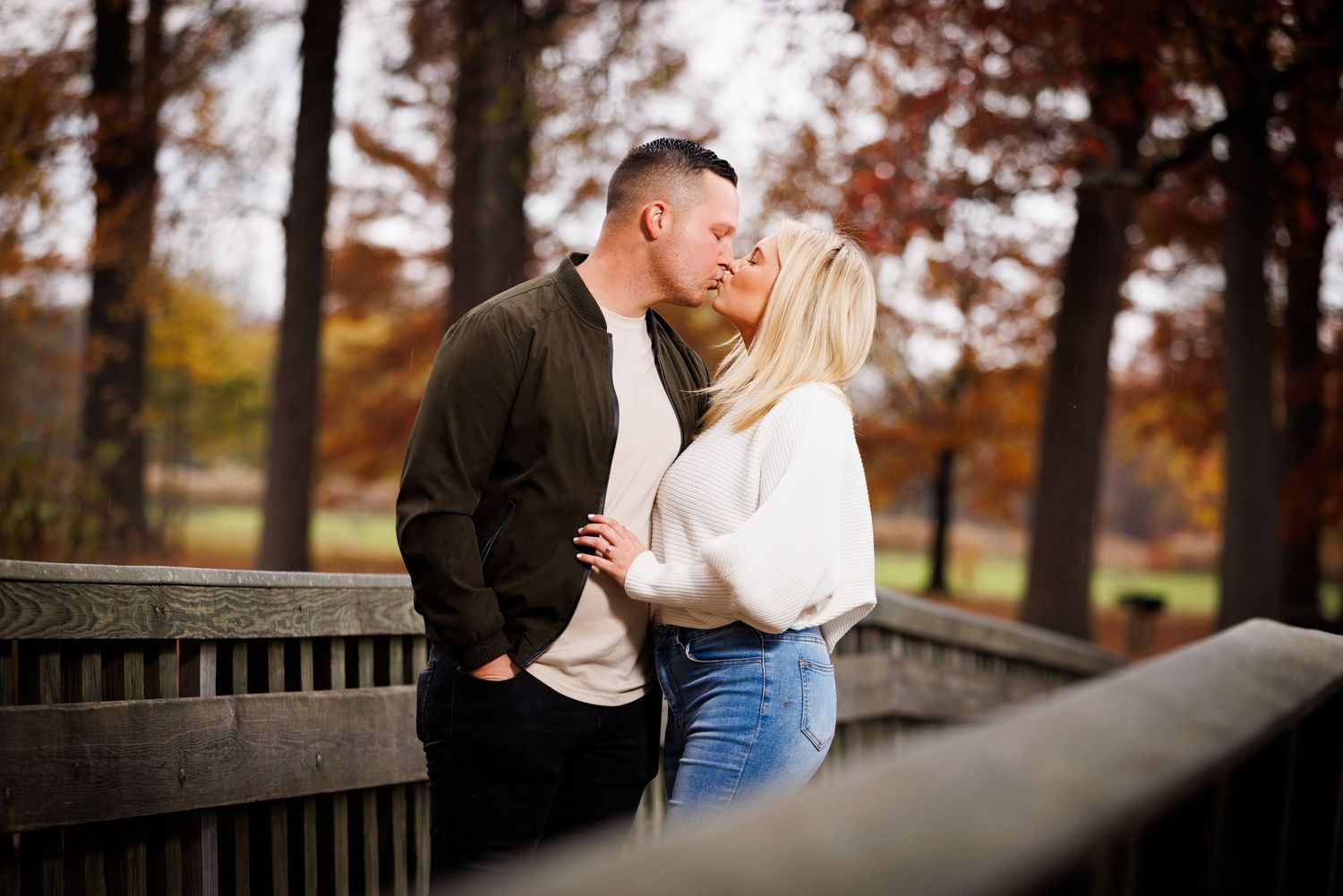 Couple kissing while leaning against a wooden bridge railing in autumn park.