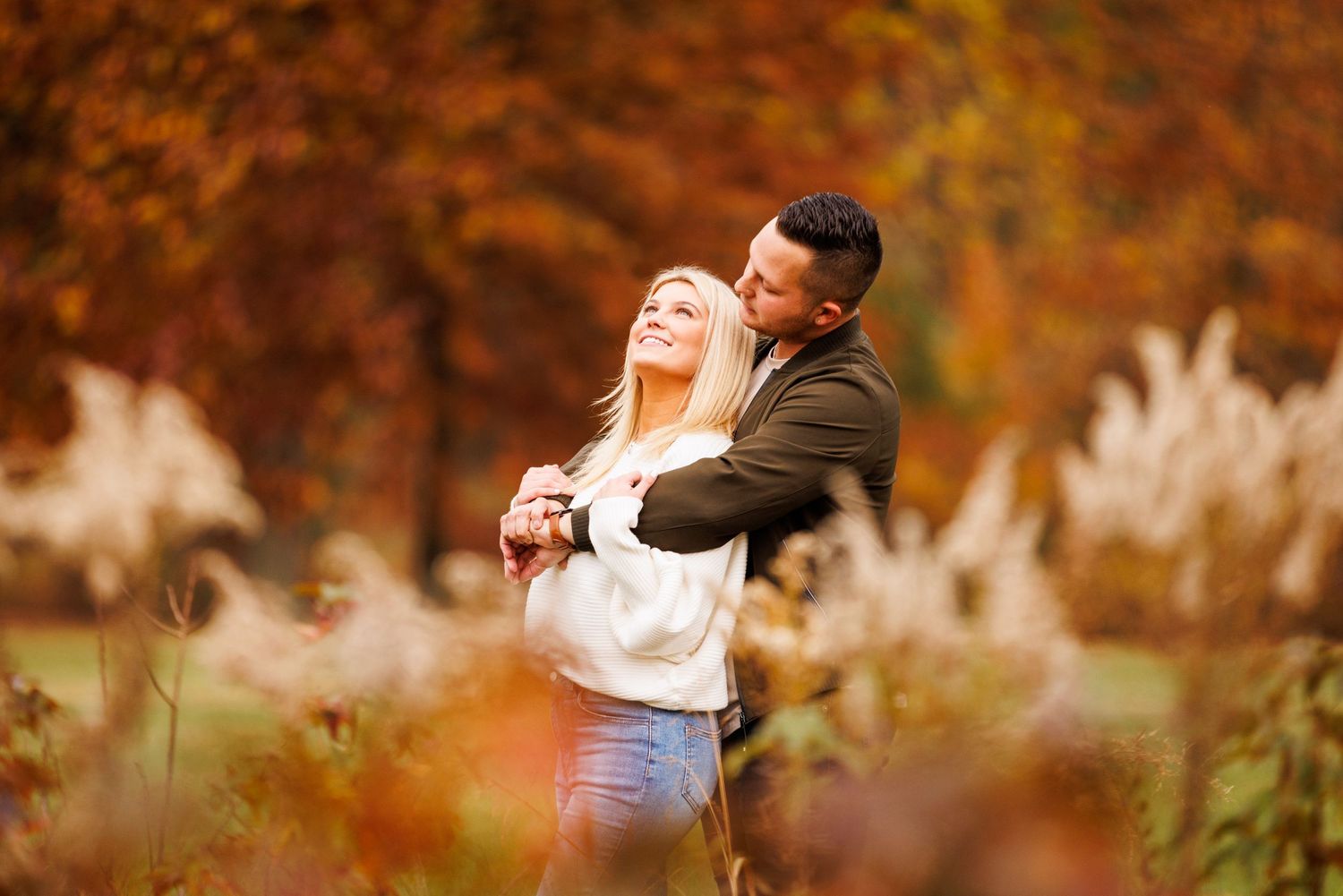 Happy couple embracing and laughing in an autumn park with golden and red foliage behind them.