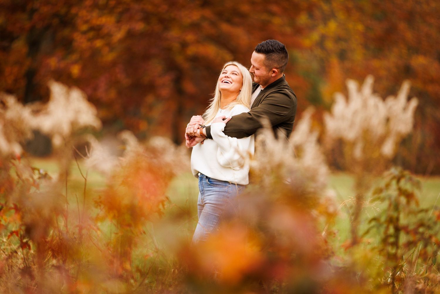 Joyful couple dancing together outdoors surrounded by stunning orange and red fall foliage.