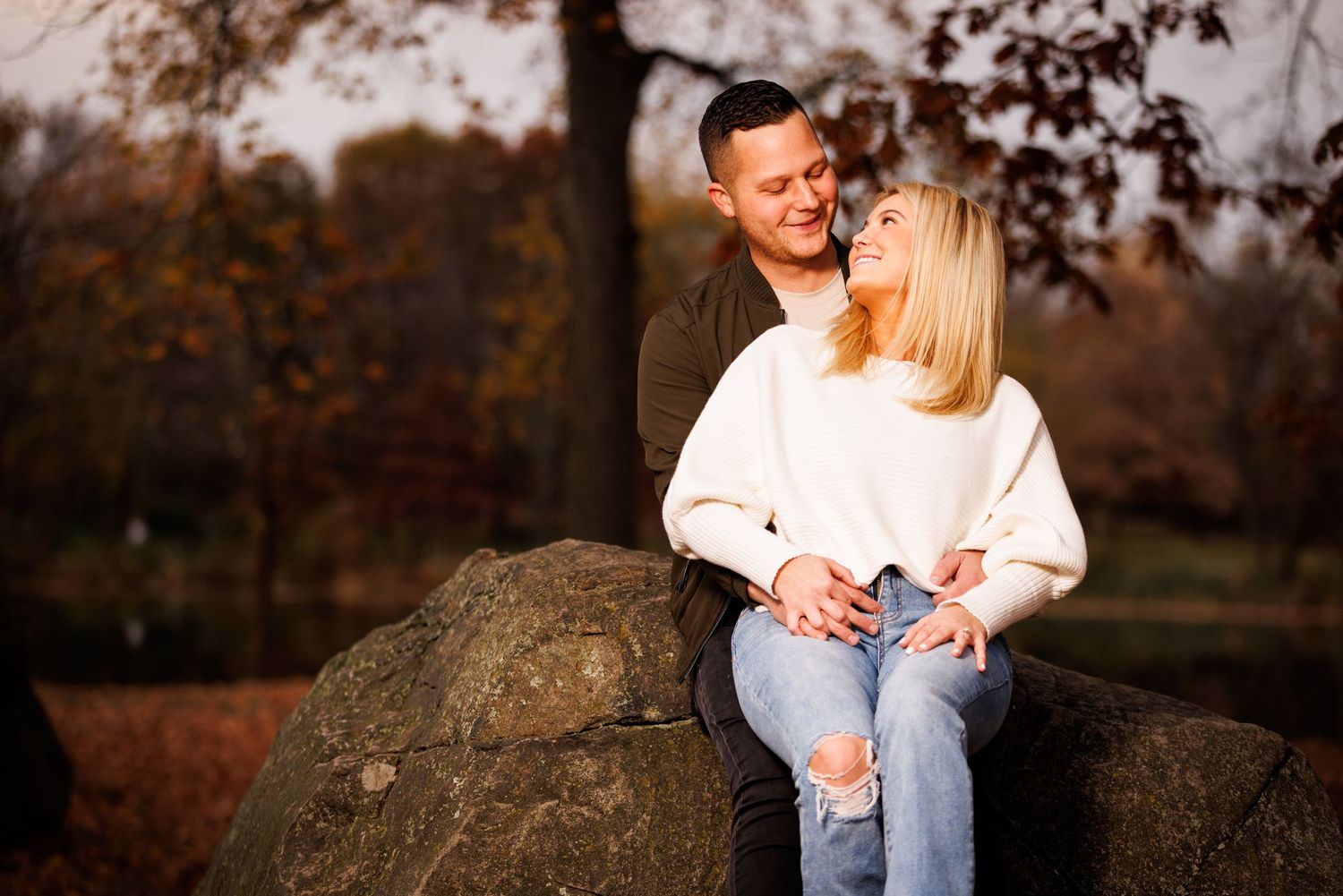 Romantic couple sitting on large rocks in an autumn park, smiling and gazing at each other.