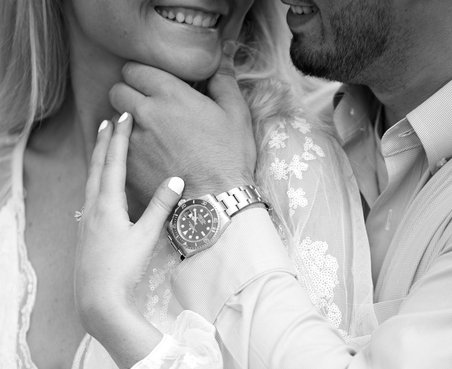 Black and white close-up of a couple embracing, man wearing a silver watch, woman in a lace white dress.