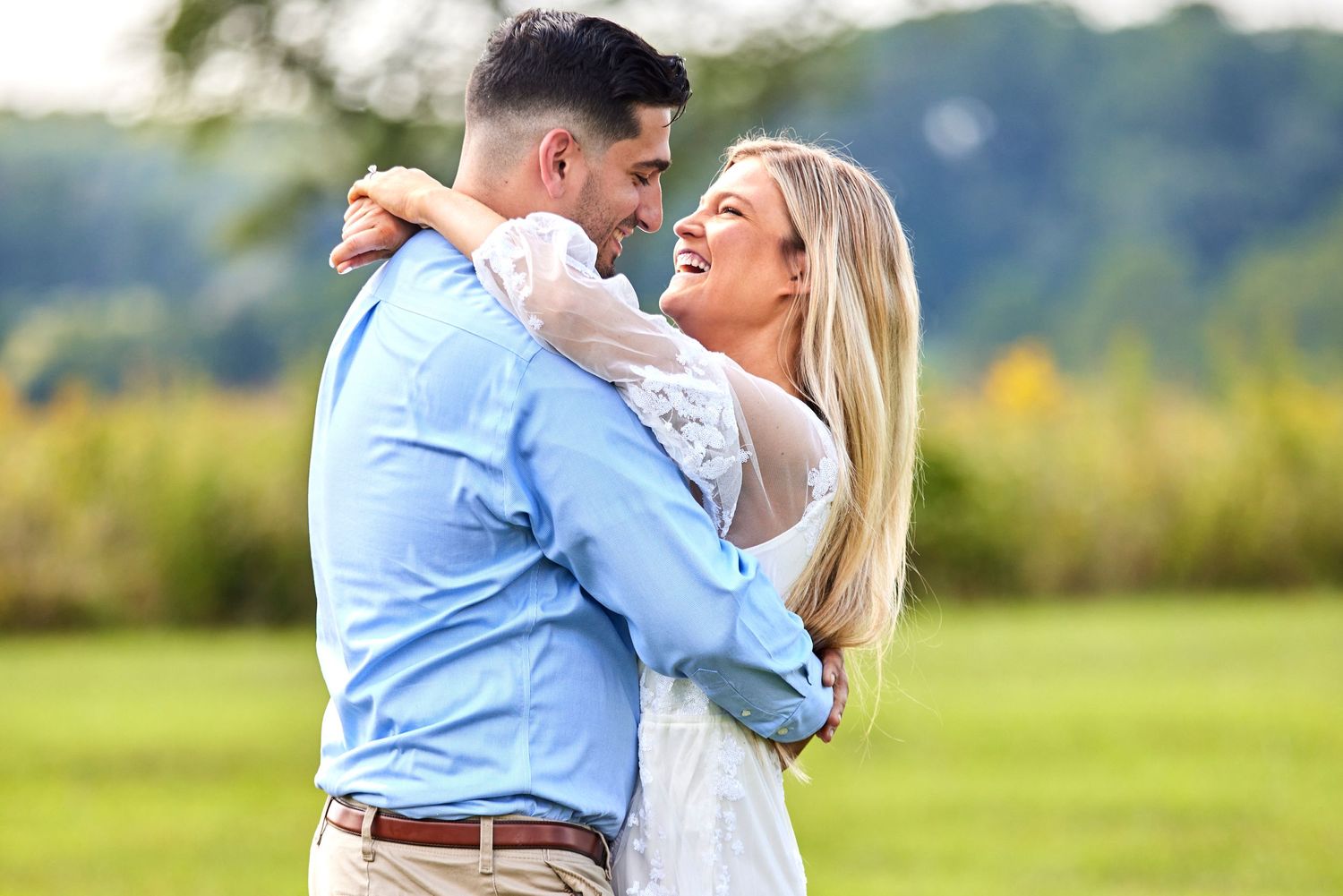 Happy couple embracing and laughing together in a green outdoor field during an engagement photo session.
