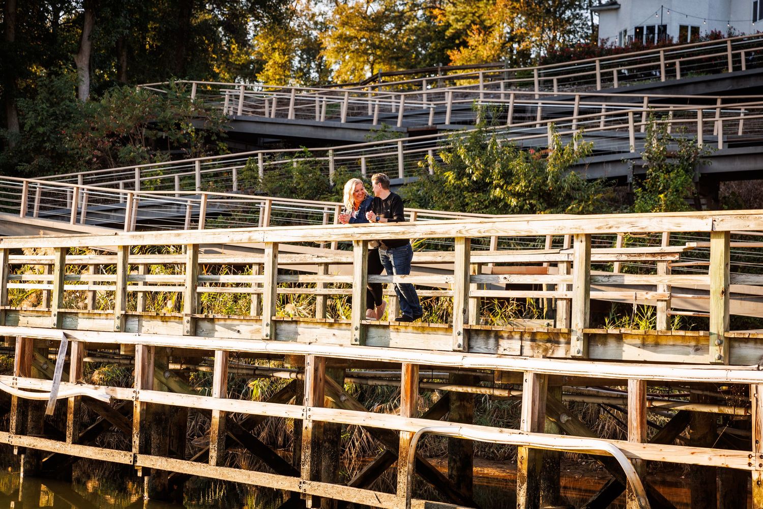 Couple embracing on a wooden bridge over water surrounded by autumn foliage.