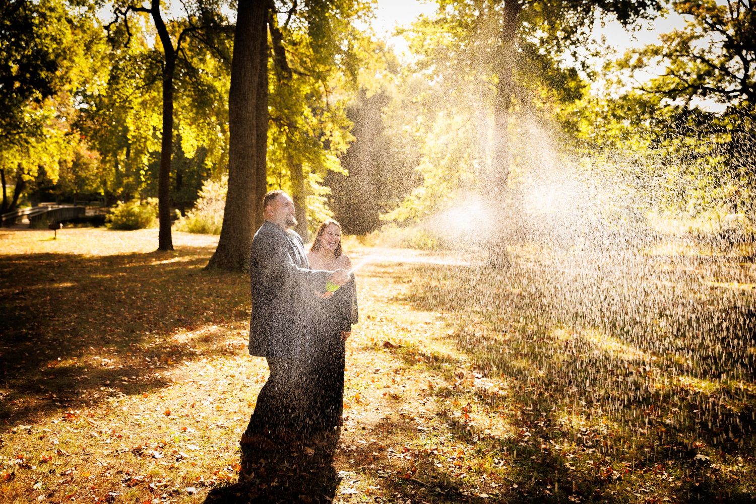 Couple embracing in a sunlit autumn park with golden light rays and falling leaves around them.