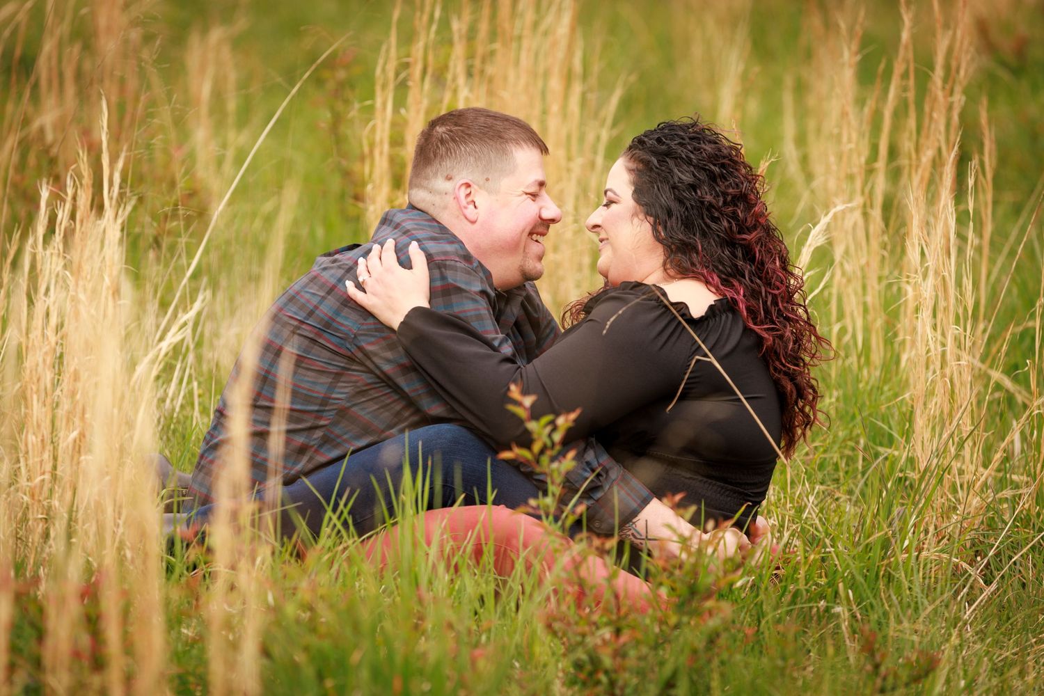 Romantic couple embracing and gazing at each other while sitting in a lush green grass field.