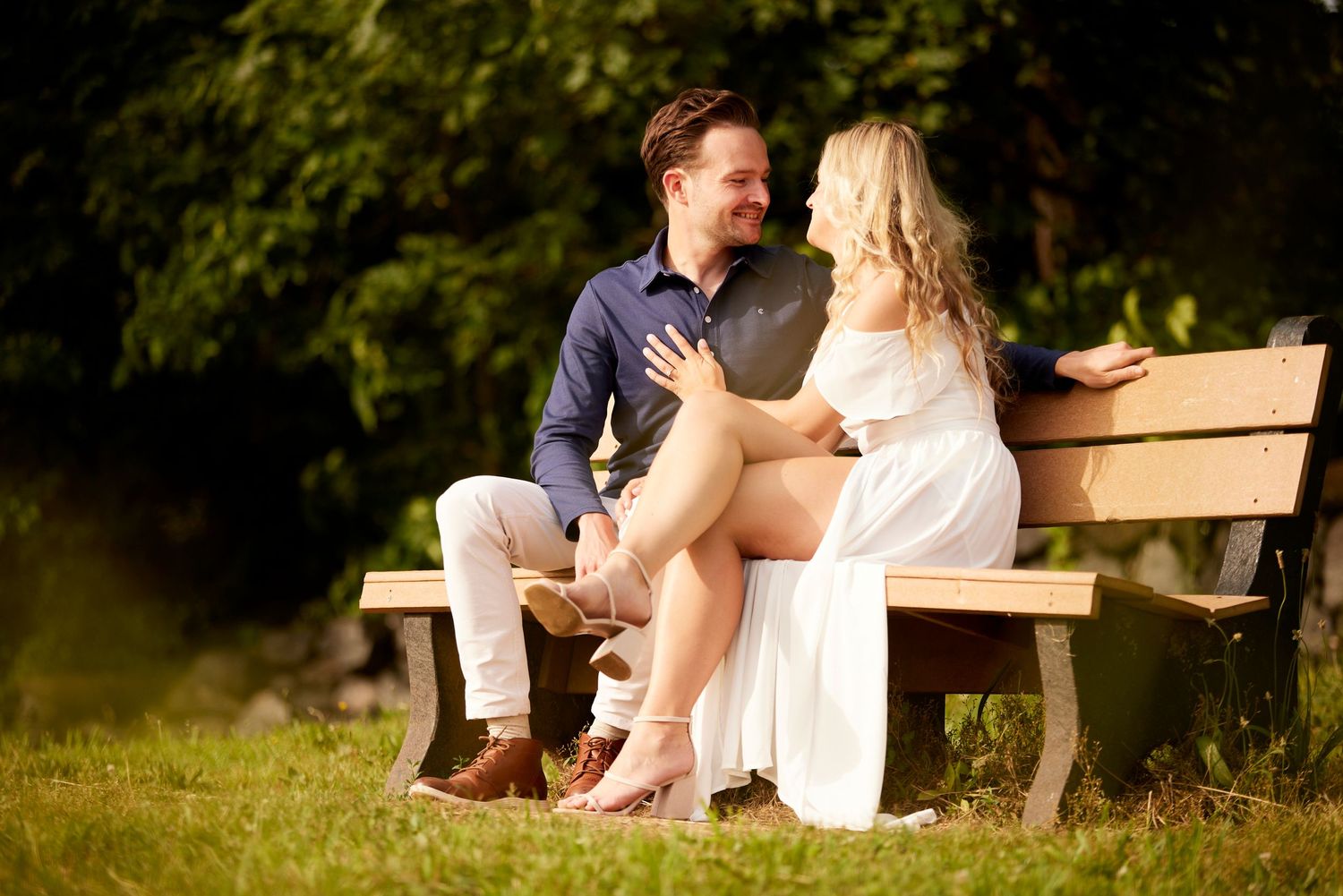 Couple sitting together on a park bench in warm sunlight during a romantic engagement session.