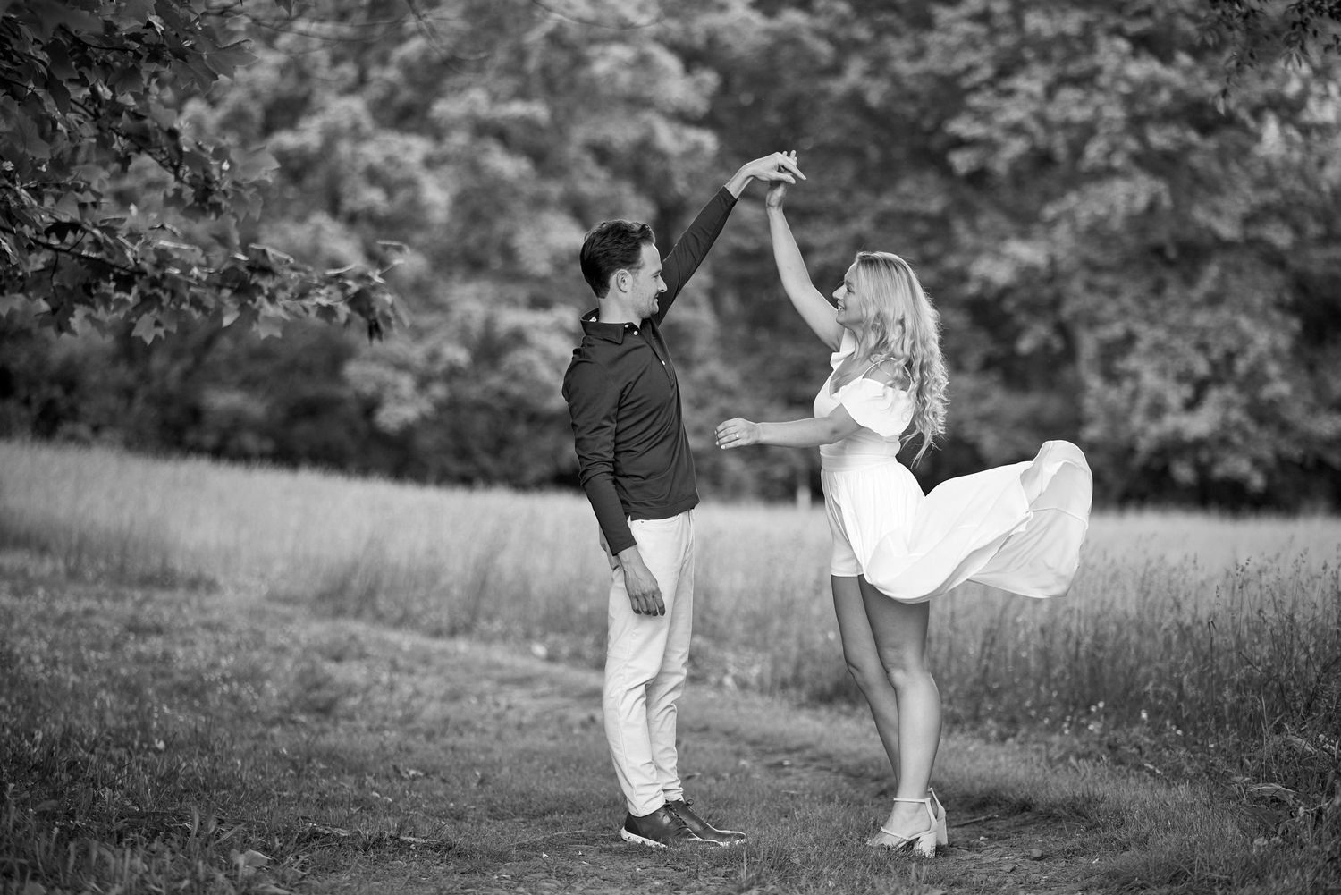 Black and white photo of a couple dancing and spinning together in a lush green outdoor field.