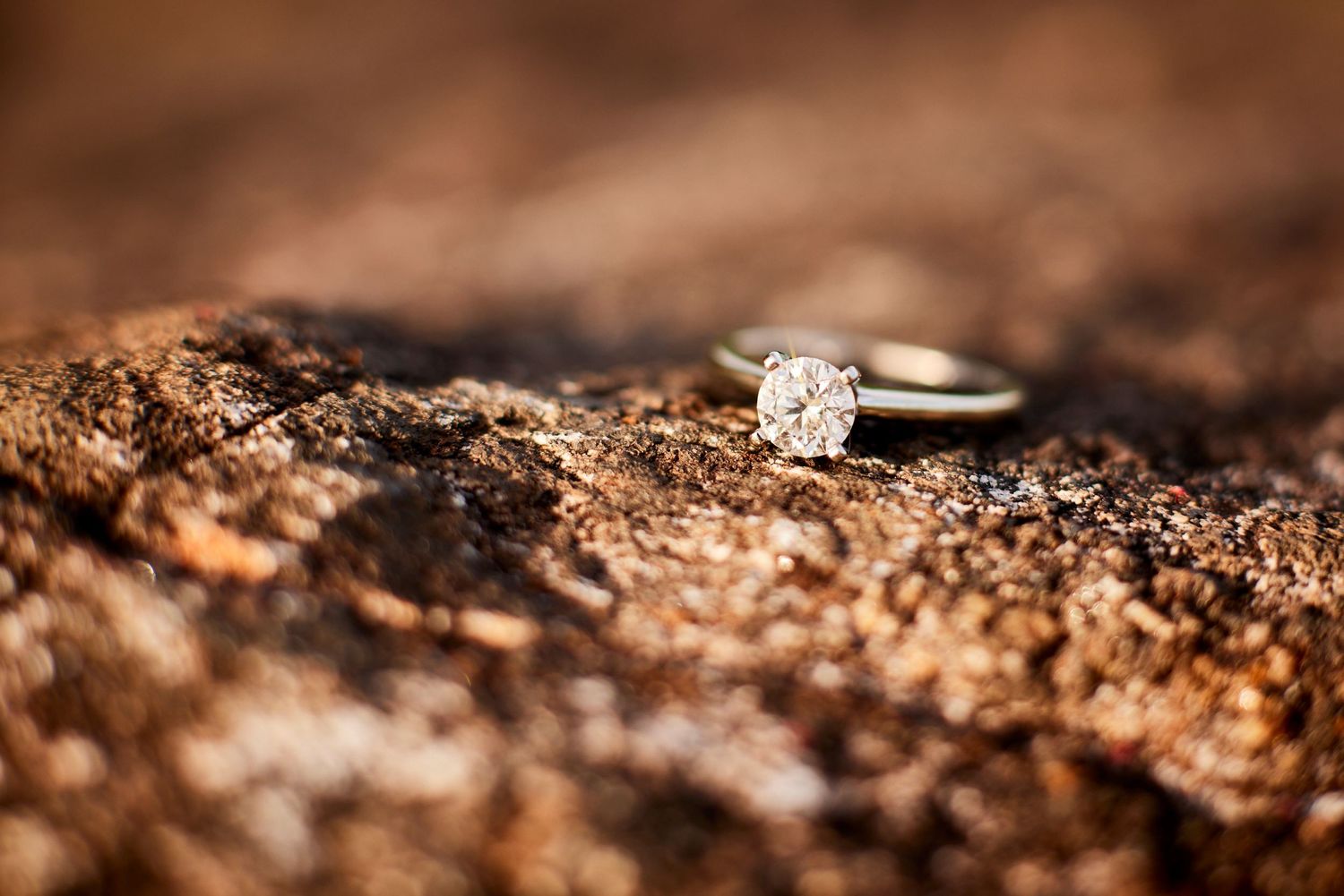 Close-up of a sparkling diamond solitaire engagement ring resting on a rustic textured rock surface.
