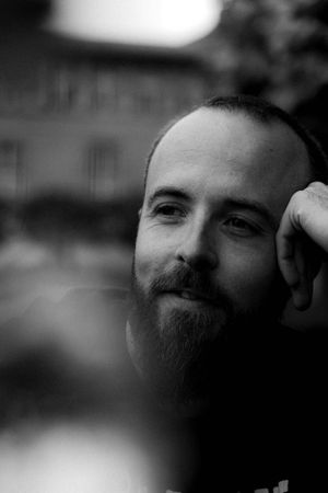 Black and white portrait of a bearded person in contemplative pose.