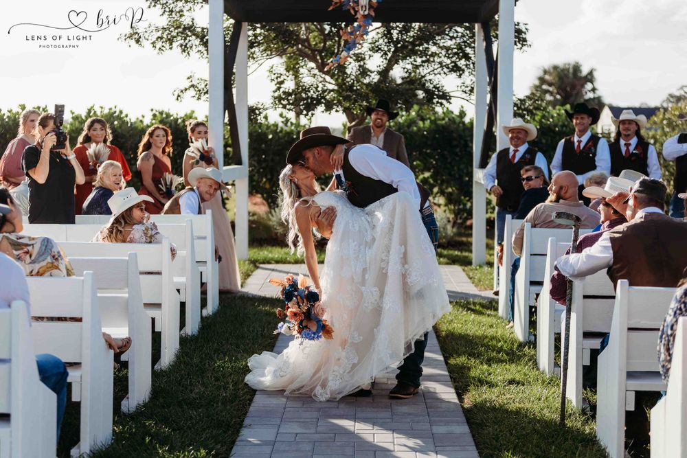 Romantic moment captured during outdoor wedding ceremony with white chairs and floral arrangements.