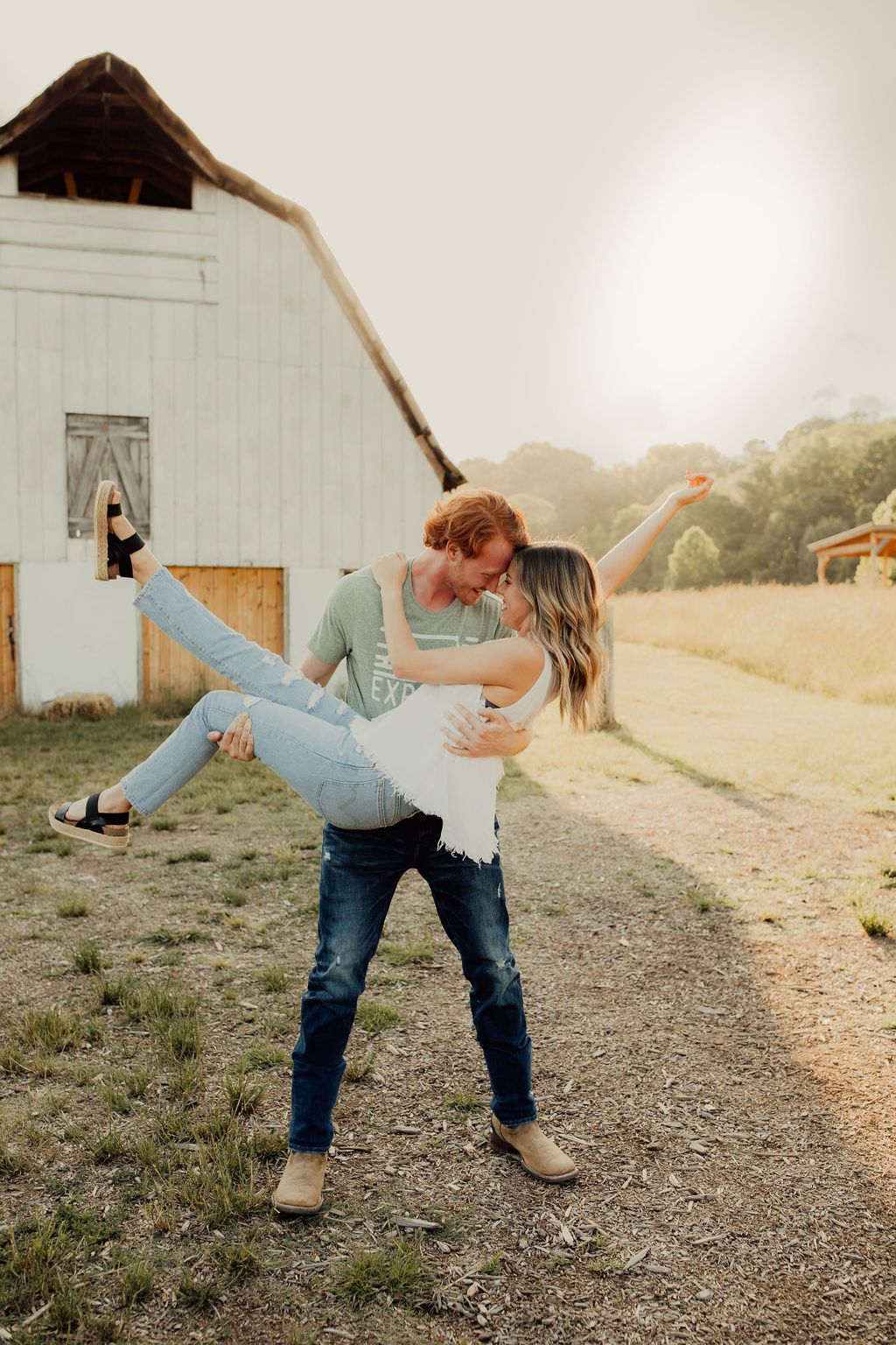 A romantic moment captured in front of a rustic white barn during golden hour.