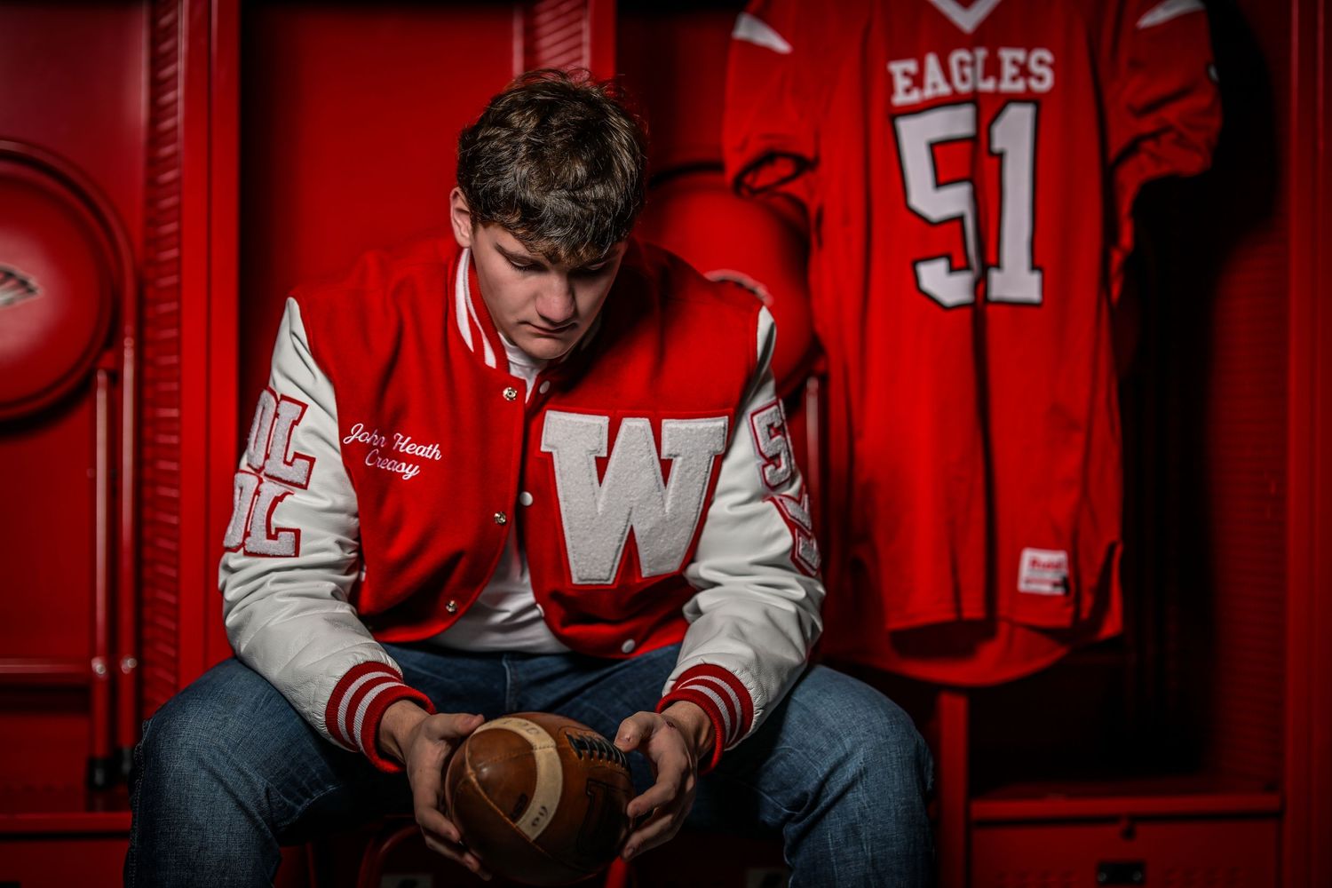 A varsity letterman in red and white sits solemnly in a sports locker room.