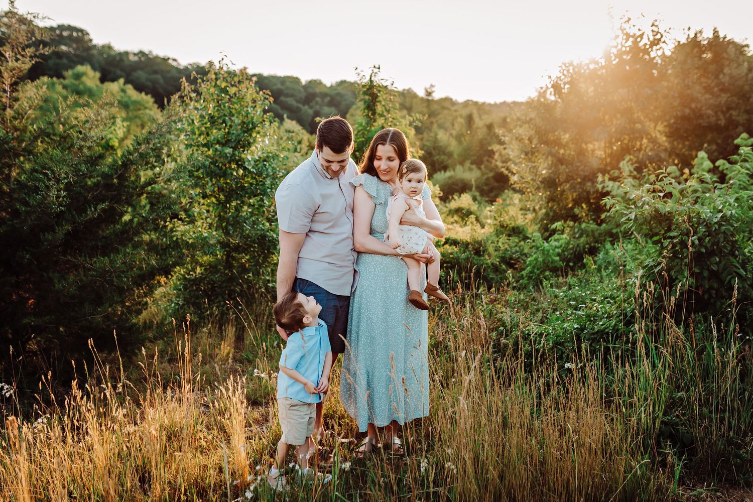 Family standing together in golden field during sunset photoshoot.