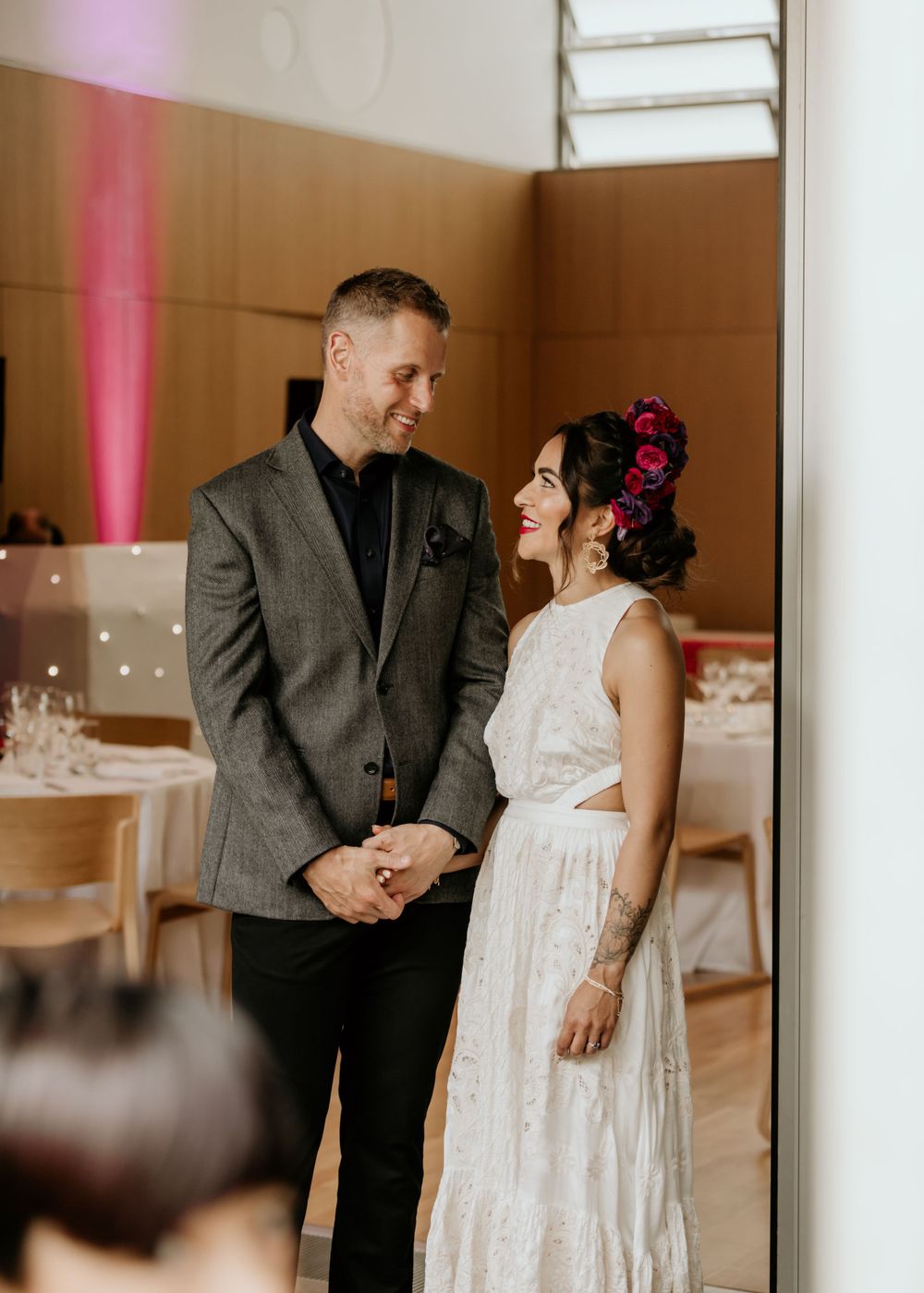 A couple shares an intimate moment in a wedding venue with the bride wearing a white lace dress and floral crown.